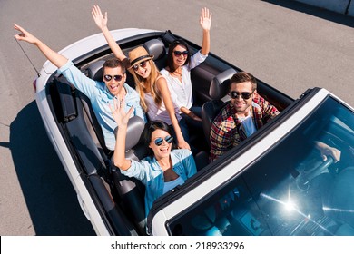 Traveling with fun. Top view of young happy people enjoying road trip in their white convertible and raising their arms