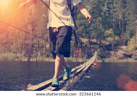 Traveling man crossing through hanging bridge in good sunny day over the lake (intentional sun glare, lens flares and vintage color)