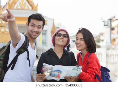 Traveling Man Woman And Senior Tourist Holding Travel Guide Book In Hand Pointing To Destination For Visiting 