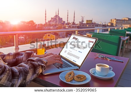 Traveling Person working on Laptop Computer at Roof Top Cafe sitting at table with Coffee Cookies and orange Juice Istanbul city Landscape on background Morning Sunlight