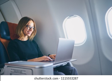 Traveling and technology. Flying at first class. Pretty young businees woman working on laptop computer while sitting in airplane.