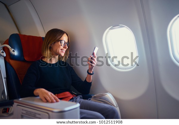Traveling and\
technology. Flying at first class. Pretty young businees woman\
using smartphone while sitting in\
airplane.