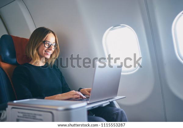 Traveling and technology. Flying at first\
class. Pretty young businees woman working on laptop computer while\
sitting in airplane.