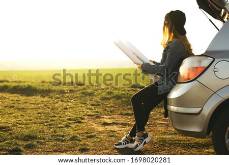 Traveling young girl looking at the right direction on the map in the trunk of the car. Concept of freedom and active lifestyle, adventure, travel.