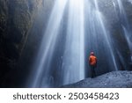 Traveller at seljalandsfoss cascade posing under water stream, river raining over tourists inside of icelandic waterfall. Frozen cold flow near mountain tops and cliffs, majestic scenery.