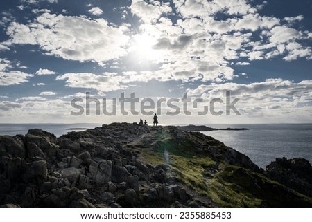 Traveller taking a picture with a cell phone on a rocky shoreline overlooking the Atlantic Ocean in Newfoundland Canada.
