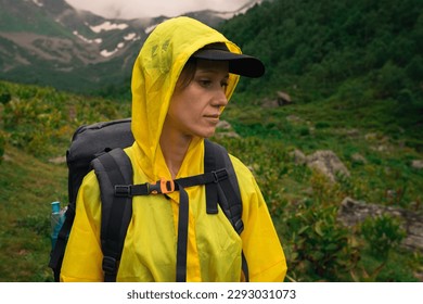 Traveller woman in yellow raincoat hiking in mountain valley in rainy day. City escape and exploring scenic nature landscape - Powered by Shutterstock