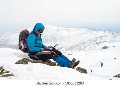 Traveller Working With A Laptop In Winter On Top Of A Mountain During The Snowstorm