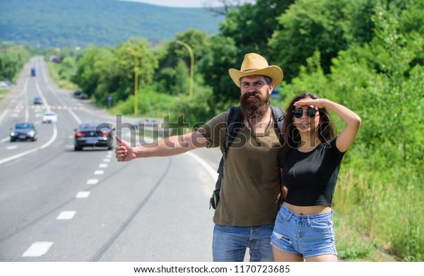 Travellers try to stop car. Hitchhiking is\
one of cheapest ways of traveling. Couple hitchhikers travelling\
summer sunny day. Couple travelers man and girl hitchhiking at edge\
road nature\
background.