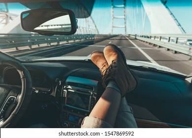 Travellers's Feet In Boots On Car Dashboard. Looking Forward At Road Throught Windshield. POV Freedom Trip Concept.