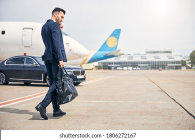 Travelling businessman talking on the phone carrying a bag while walking outside airport