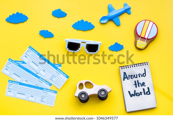 Travelling with child concept. Air balloon, car and\
plane. Around the world hand lettering in notebook on yellow\
background top view copy\
space