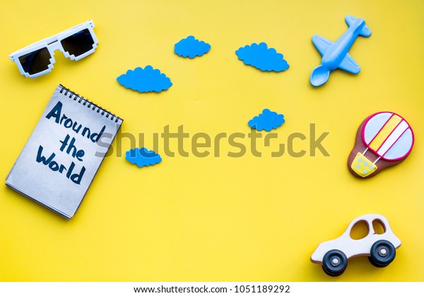 Travelling with child concept. Air balloon, car\
and plane. Around the world hand lettering in notebook on yellow\
background top view copy\
space.