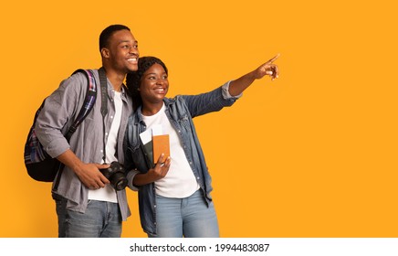 Travelling Concept. Young Black Tourists Couple Holding Pasports And Photo Camera And Pointing Aside, Excited African Lovers Ready For Vacation Journey, Isolated On Yellow Background, Panorama