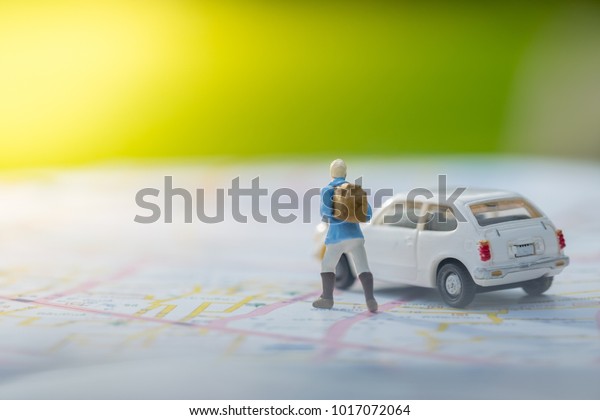 Travelling concepts. 
Traveler miniature mini figures with backpack standing with white
car model on map