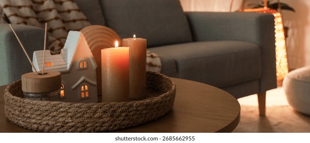 Tray with burning candles and reed diffuser on table in living room at night