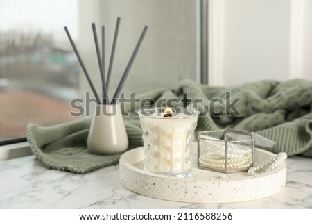 Tray with burning soy candle and beautiful bijouterie on white window sill indoors
