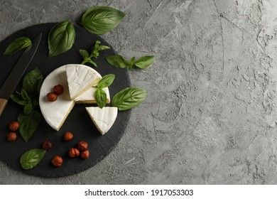 Tray with camembert, hazelnut, basil and knife on gray background