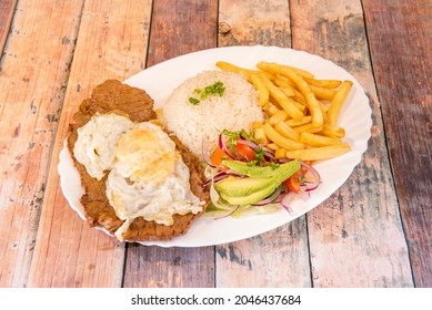 Tray Of Ecuadorian Churrasco With Beef Steak, Fried Egg On Top And Various Garnishes Of French Fries, White Rice And Avocado With Purple Onion Salad