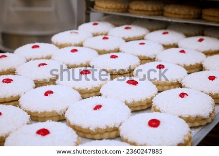tray full of cakes with coconut topping and cherry on top sat on a baking tray.  