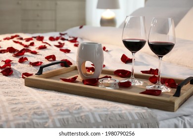 Tray With Glasses Of Red Wine, Candles And Rose Petals On Bed In Room