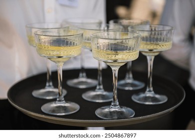 Tray of glasses of summer sparkling wine for guests at wedding reception. The waiter serving champagne on tray. Waiter holding glasses in backyard. Woman brings full glasses of champagne closeup. - Powered by Shutterstock