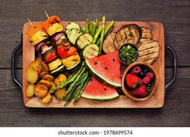 Tray Of Grilled Vegan Bbq Food. Top View Over A Dark Wood Background. Grilled Vegetables, Fruit And Skewers. Healthy Summer Meat Substitute Concept.