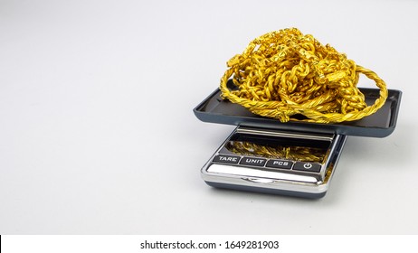 A tray of ladies shining gold jewellery on a digital weighing scale with white background. The scale is on the right side of the photo. 