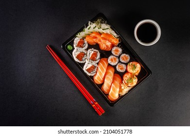 Tray sushi salmon varieties for delivery: sashimi, onigiri, sushi Jhow, sakemaki and uramaki philadelphia with shoyu and chopsticks on a blackbackground. Top view.