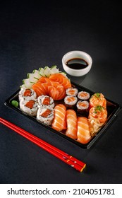 Tray sushi salmon varieties for delivery: sashimi, onigiri, sushi Jhow, sakemaki and uramaki philadelphia with shoyu and chopsticks on a blackbackground.