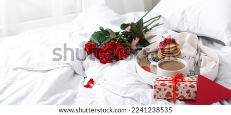 Tray with tasty breakfast, bouquet of roses and gift for Valentine's Day on bed