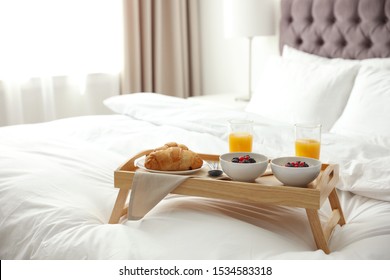 Tray with tasty breakfast on bed in light room