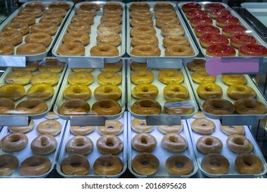 Trays full with delicious glazed donuts placed on a shelf inside a glass display cabinet. No focus, specifically.