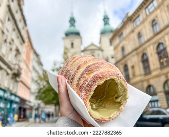 trdelnik, traditional old Bohemian sweet pastry made of yeast dough. Trdelnik is unique cinnamon sugar pastry found throughout Prague, Czech republic. selective focus on dessert over city landmarks - Shutterstock ID 2227882365