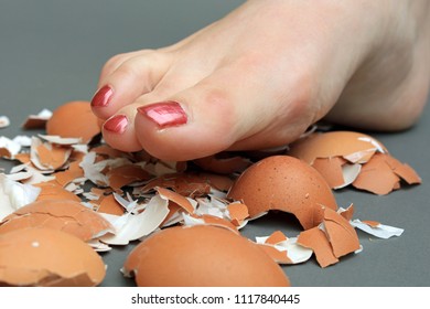 Treading On Eggshells. Close Up Of A Barefoot Walking On Broken Egg Shells. Concept Of A Well Known Saying.