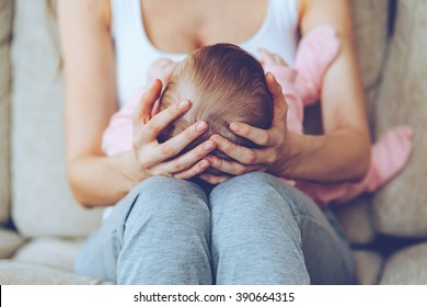 Treasure In Her Hands. Close Up Part Of Young Woman Holding Baby Girl On Her Knees While Sitting On The Couch 