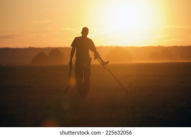 Treasure Hunter With Metal Detector In The Field On The Sunset