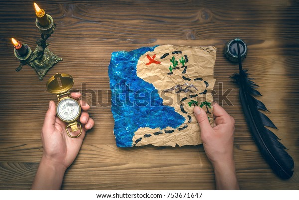 Treasure map ,hand and\
compass on wooden table. Treasure hunt background. Adventurer man\
holding in one hand compass and treasure map in another hand and\
research it.