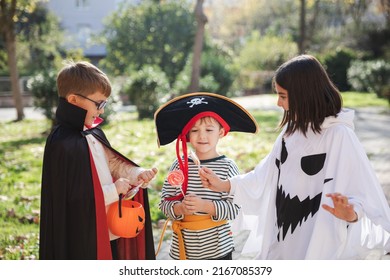 Treat or trick! Happy kids wearing carnival costumes of ghost, pirate and vampire for Halloween celebration sharing candies with each other staying in the park. - Powered by Shutterstock