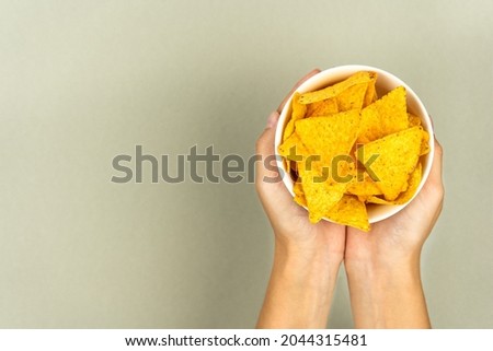 Treating crispy nachos chips in a plate and female hands on a colored background.