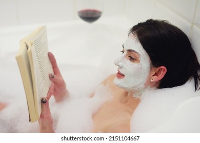 Treating Herself To Some Time In The Tub. Cropped Shot Of A Young Woman Relaxing In The Bathtub With A Book And Glass Of Wine.