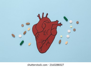 Treatment Of Cardiovascular Disease Concept. Paper Cut Anatomical Heart With Stethoscope And Pills On A Blue Background. Top View