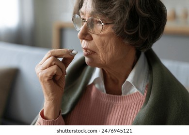 Treatment, medication at retirement. Elderly woman taking pill, senior lady holding hand with medicine near mouth - Powered by Shutterstock