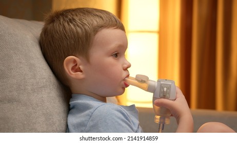 Treatment Of Pneumonia With Nebulizer At Home. Child Has Respiratory Infection Or Bronchitis, And He Is Breathing Heavily. Blond Caucasian Child With Asthma Problems Inhales With Tube In His Mouth.