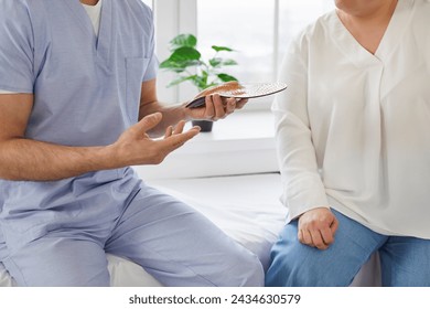 Treatment and prevention of flat feet and orthopedic foot diseases. Doctor in clinic advises patient about individual orthopedic insoles for correction of flat feet. Cropped image, selective focus.