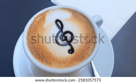 
Treble clef pattern on coffee foam. A cup of aromatic coffee with a treble clef pattern. Classical music notes treble clef. Musical mood. Delicious coffee.