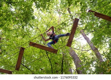 Tree Adventure Park. Young Girl Climbing In Trees On Ropes Image Shot From Below Looking Up At Tree Tops.