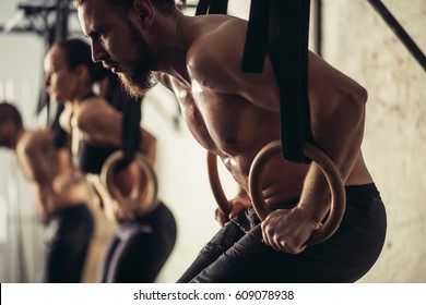 Tree Attractive Young Male And Female Adults Doing Pull Ups On Bar In Cross Fit Training Gym With Brick Walls And Black Mats