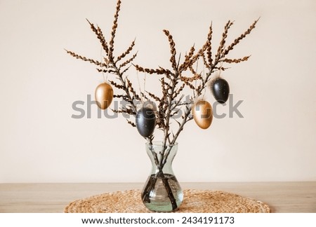 Tree branches in vase with colored Easter eggs hanging on string. Nice warm beige earthly tones. Minimal home Easter decoration.