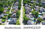 Tree lined residential street with well-trimmed front yard of upscale two-story suburban houses with swimming pool, large fenced backyard, well-trimmed HOA landscape, Dallas, Texas, aerial view. USA